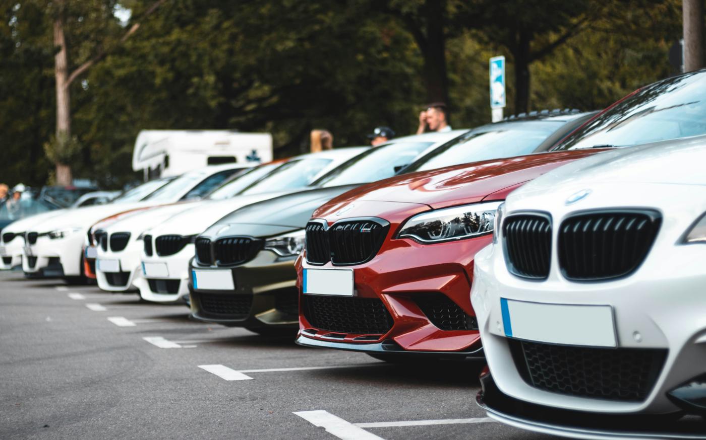 A row of parked cars including white, olive, and red sedans in a lot by Sara Kurfeß courtesy of Unsplash.