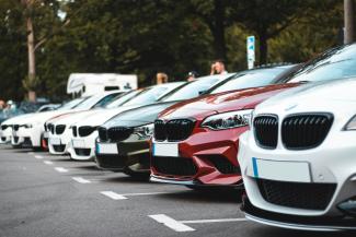 A row of parked cars including white, olive, and red sedans in a lot by Sara Kurfeß courtesy of Unsplash.