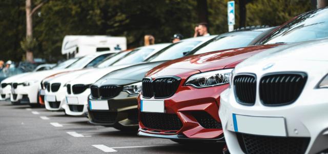 A row of parked cars including white, olive, and red sedans in a lot by Sara Kurfeß courtesy of Unsplash.